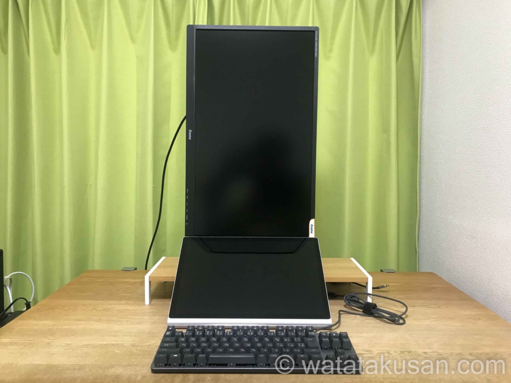 ニトリのラックヴィトの上にモニターを縦向きでのせ、Surfacebook2、有線のキーボードを置いている。